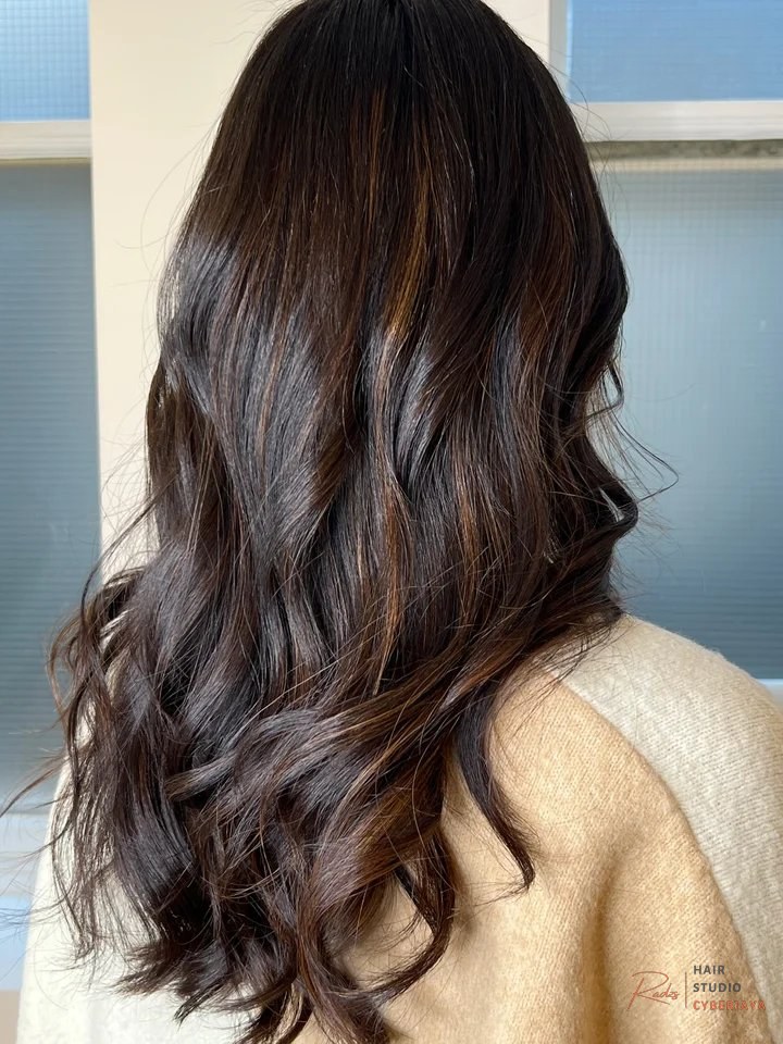 I Got 'Candlelit Brunette' Hair For Winter & I Love It A woman with a unique and stylish hair color featuring vibrant pink and purple pastel shades artfully blended into her dark hair.